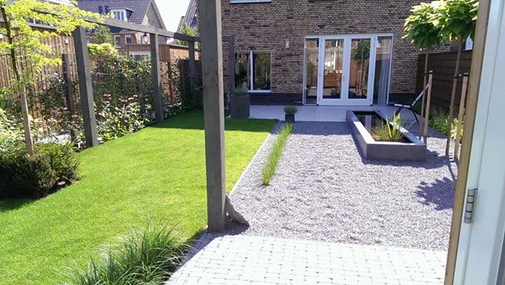 Achtertuin met gazon, een grindpad en een pergola