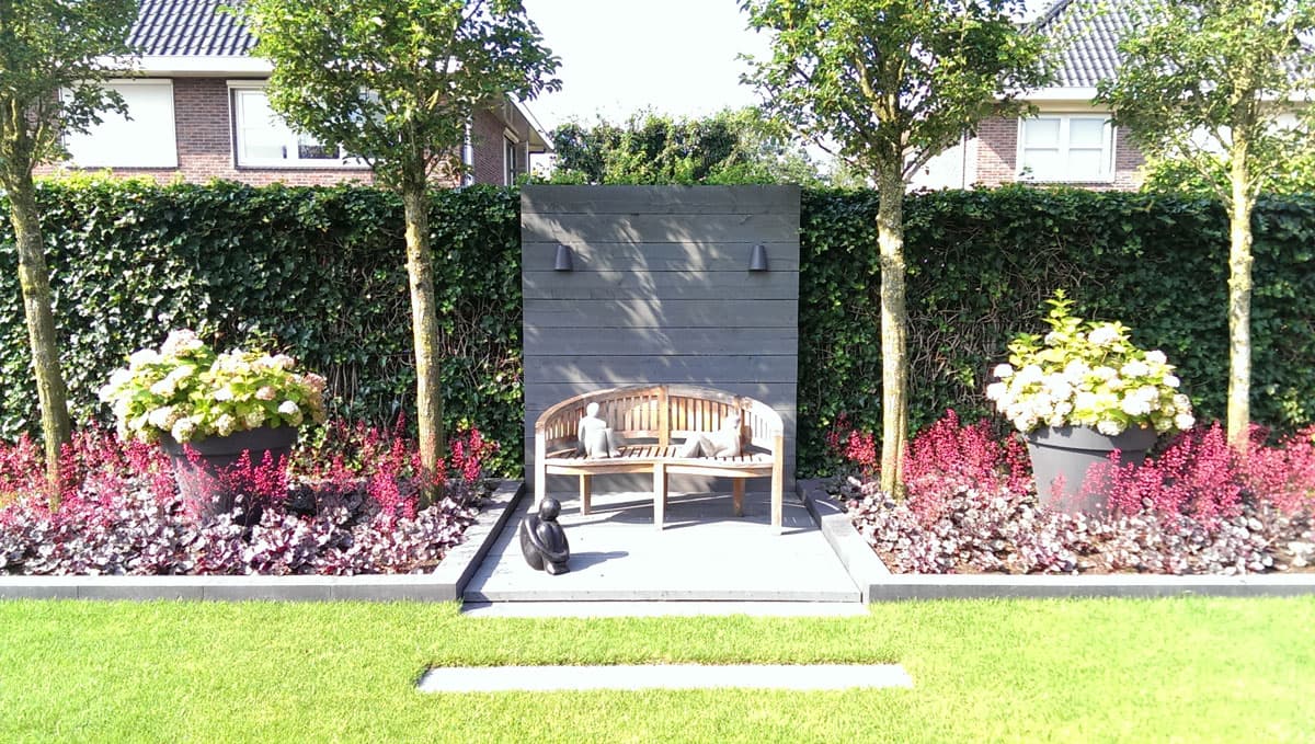 Moderne tuin met een bankje tegen een donkere wand en bloeiende borders