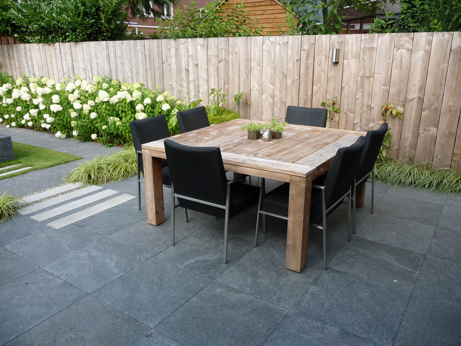 Aangelegd terras met eettafel, witte hortensia's en een houten schutting